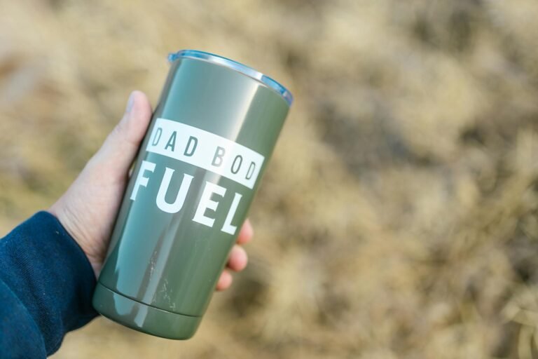Green tumbler with 'Dad Bod Fuel' text held outdoors. Perfect for coffee or tea lovers.
