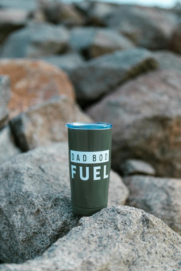 Insulated tumbler with 'Dad Bod Fuel' text placed on rocks outdoors, symbolizing rugged style.