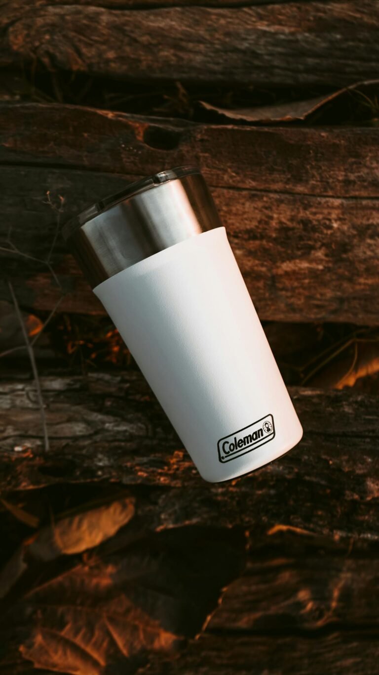 White insulated tumbler resting on wooden logs, ideal for camping enthusiasts.
